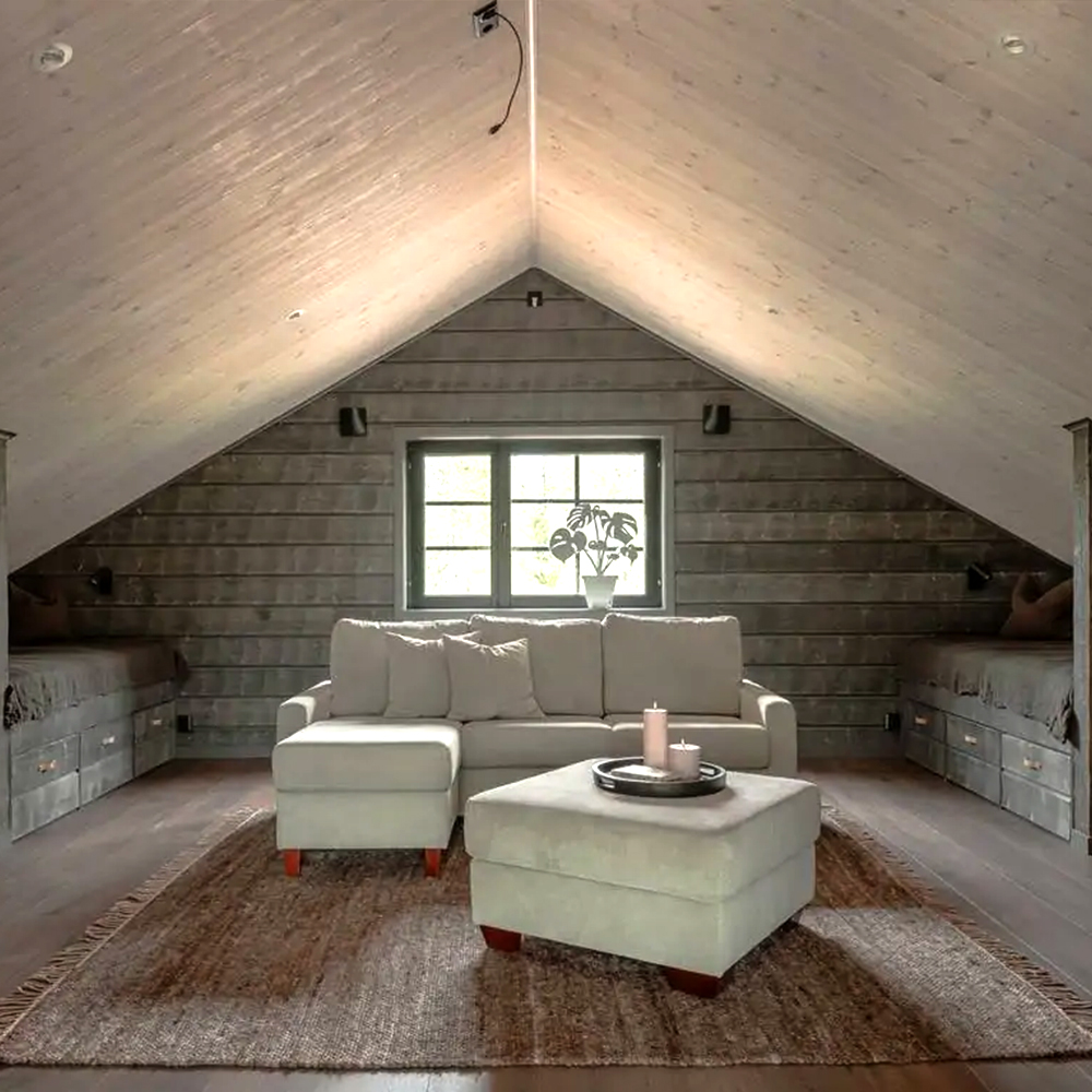 Loft med soffgrupp, platsbyggda sängar och stort fönster.