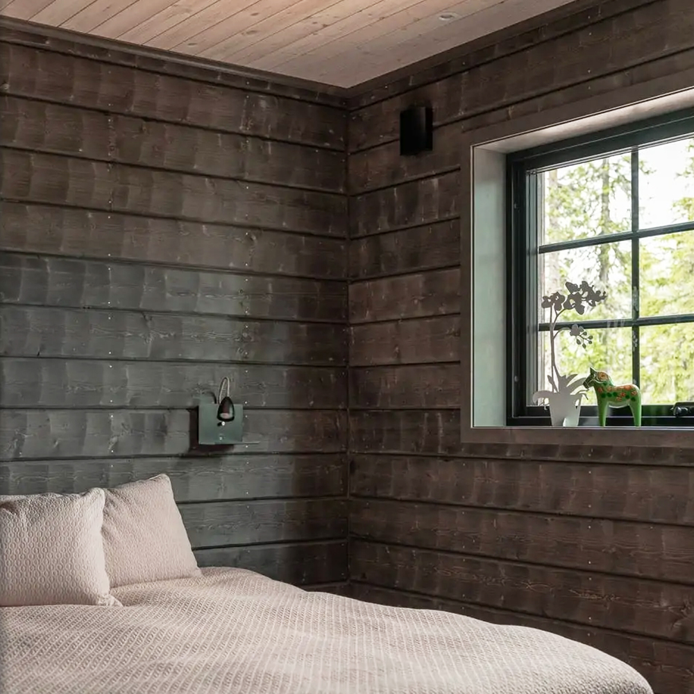 Sovrum i fjällhus med timmerpanel och stort fönster.